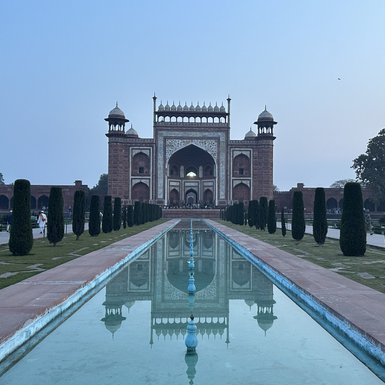Der majestätische Eingang des Taj Mahal spiegelt sich in einem ruhigen Wasserbecken, umgeben von gepflegten Hecken.