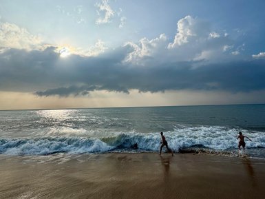 Zwei Kinder laufen am Strand entlang, während die Wellen sanft an den Ufer schlagen und der Himmel bewölkt ist.