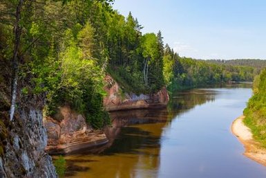 Ein ruhiger Fluss schlängelt sich durch eine grüne Landschaft, umgeben von hohen Bäumen und sanften Hügeln.