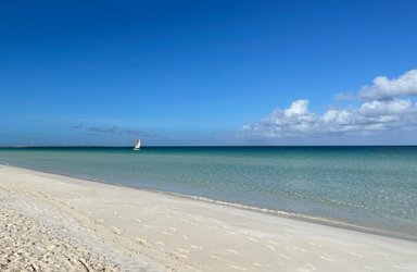 Ein ruhiger Strand mit feinem, hellem Sand und sanften Wellen, die an die Küste plätschern, unter einem strahlend blauen Himmel.