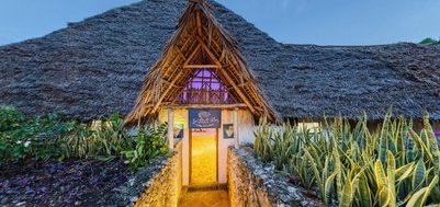Der Eingang zum Grand Bleu Restaurant zeigt eine einladende Atmosphäre mit einem strohgedeckten Dach und bunten Pflanzen.