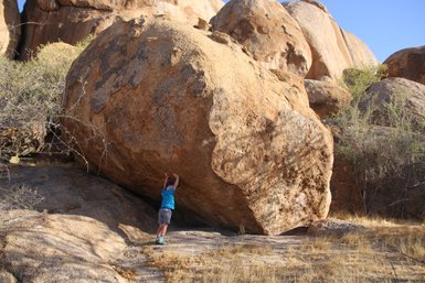 Ein Kind deutet an, einen großen Felsen zu stemmen - Namibia Urlaub mit Kindern