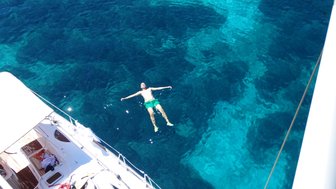 Ein Mann schwebt entspannt im klaren, blauen Wasser, während ein Boot im Hintergrund sichtbar ist.