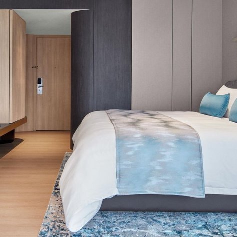 Ein modernes Hotelzimmer mit einem großen Bett, blauen Kissen und einem eleganten Schreibtisch im Hintergrund.