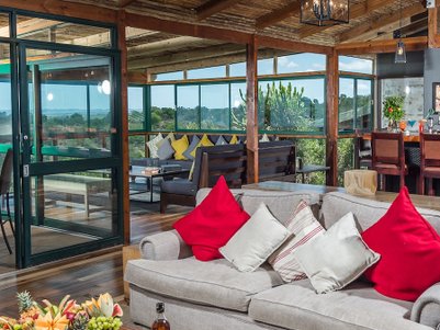 Ein einladender Lounge-Bereich mit gemütlichem Sofa, bunten Kissen und Blick auf die umliegende Natur durch große Fenster.