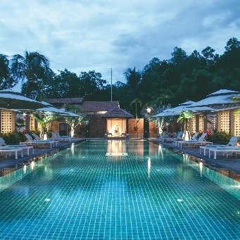 Ein ruhiger Pool in einem Resort, umgeben von Palmen und Sonnenliegen, unter einem bewölkten Abendhimmel.