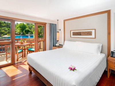 Ein helles Hotelzimmer mit einem großen Bett, das mit einer Blume dekoriert ist, und Blick auf einen Pool und Garten.