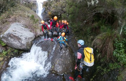 Eine Gruppe von Canyoning-Abenteurern steht an einem Wasserfall, bereit, den nächsten Abschnitt des Flusses zu erkunden.