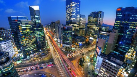 Die Stadt Seoul erstrahlt in der Dämmerung, mit leuchtenden Wolkenkratzern und lebhaften Straßen voller Autos.