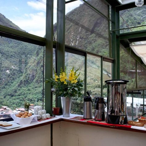 Ein einladender Frühstückstisch mit frischen Brötchen, Kaffee und einer schönen Blumendekoration, umgeben von grünen Bergen.