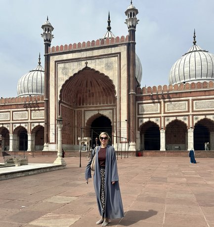 Eine Frau in einem grauen Gewand steht vor der beeindruckenden Moschee mit großen Kuppeln und kunstvollen Verzierungen.