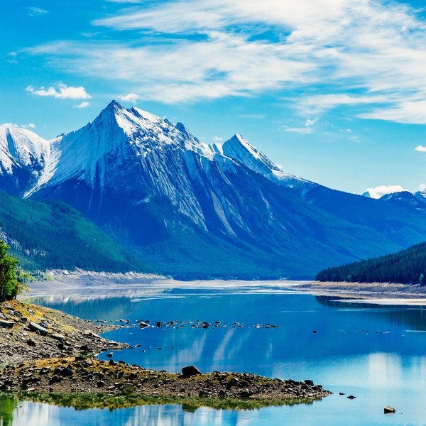 Ein klarer See spiegelt die majestätischen schneebedeckten Berge und den strahlend blauen Himmel wider.