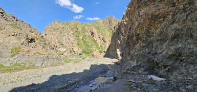 Eine schmale Schlucht mit steilen, felsigen Wänden und üppigem Grün, unter einem strahlend blauen Himmel.