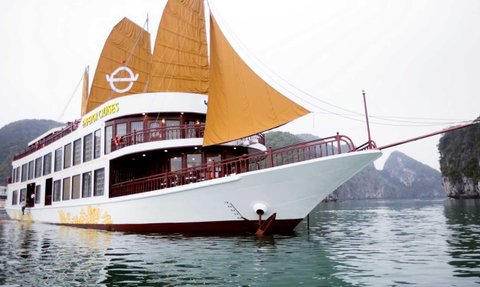 Ein elegantes Kreuzfahrtschiff mit orangefarbenen Segeln schaukelt sanft auf dem ruhigen Wasser einer malerischen Bucht.