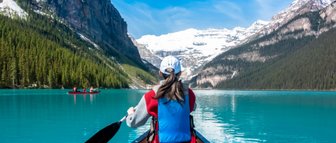 Eine Person paddelt in einem Kanu auf dem türkisfarbenen Wasser des Lake Louise, umgeben von majestätischen Bergen.