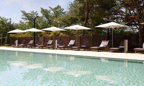 Ein ruhiger Poolbereich mit glitzerndem Wasser, umgeben von Liegen und Sonnenschirmen unter blauem Himmel.