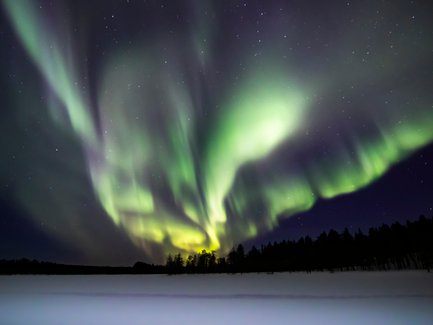 Ein atemberaubendes Nordlicht erhellt den Nachthimmel über einer verschneiten Landschaft in Finnland.