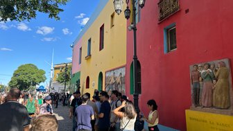 Bunte Gebäude in Buenos Aires umgeben von Menschen, die an einer belebten Straße stehen und miteinander sprechen.