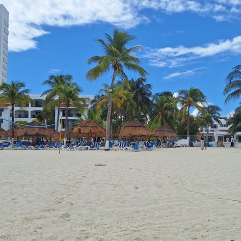 Ein sonniger Strand mit Palmen, Liegen und Strohhütten, ideal für Entspannung und Freizeitaktivitäten.