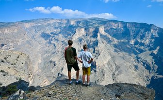 Teenager und Kind blicken gemeinsam auf die atemberaubende Schluchtlandschaft des Jebel Shams – Oman mit Kindern