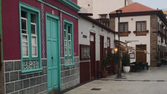 Bunte Gebäude mit einer türkisfarbenen Tür und einem gepflasterten Gehweg in einer ruhigen Straße in Puerto de la Cruz.