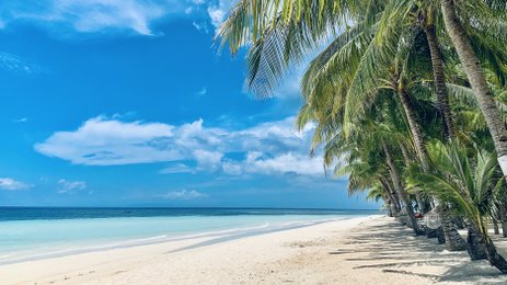 Ein ruhiger Strand mit feinem, weißen Sand erstreckt sich unter einem strahlend blauen Himmel und sanften Wolken.