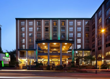 Das Holiday Inn & Suites in Vancouver zeigt eine moderne Fassade mit beleuchtetem Eingangsbereich und grünen Akzenten.