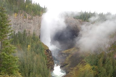 Ein majestätischer Wasserfall stürzt in eine tiefe Schlucht, umgeben von dichten, grünen Wäldern und mystischem Nebel.