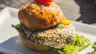 Ein köstlicher Burger mit Sesambrötchen, frischem Salat und einer roten Kirschtomate als Dekoration auf dem Tisch serviert.