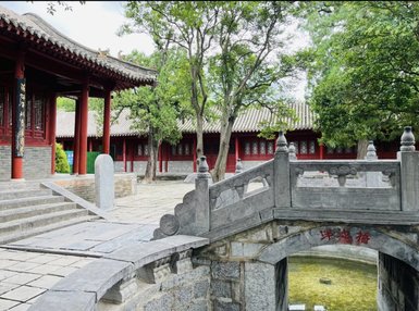 Eine steinerne Brücke führt über einen klaren Teich, umgeben von üppigem Grün und traditioneller Architektur.