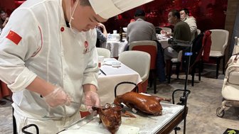 Ein Koch in einem Restaurant schneidet sorgfältig eine knusprige Pekingente auf einem Servierwagen für die Gäste.