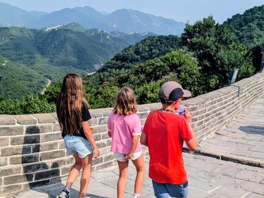 Drei Kinder erkunden die Chinesische Mauer und genießen die wunderschöne Aussicht auf die umliegenden Berge und Hügel.