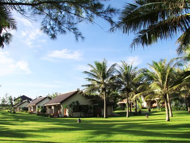 Eine ruhige Gartenlandschaft mit Palmen und charmanten Bungalows unter einem strahlend blauen Himmel.