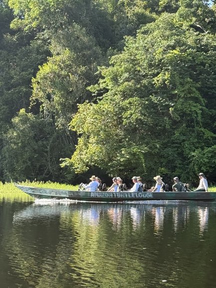 Eine Gruppe von Menschen sitzt in einem Boot und genießt die Zeit auf einem ruhigen Gewässer umgeben von dichtem Grün.