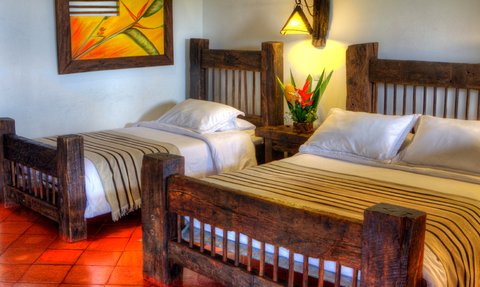 Ein gemütliches Schlafzimmer mit zwei rustikalen Holzbettgestellen und frischen Blumen auf einem Nachttisch.