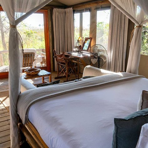 Ein gemütliches Zimmer mit einem großen Bett, umgeben von sanften Vorhängen und Blick auf die Natur durch große Fenster.