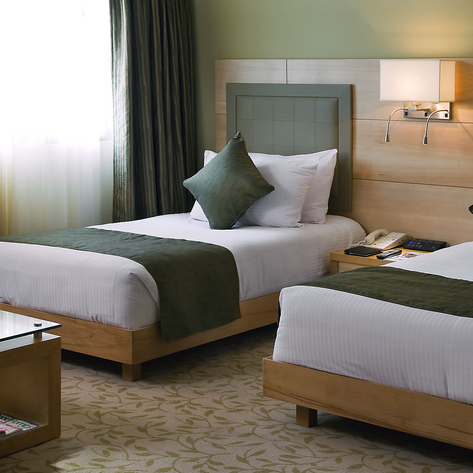 Ein elegantes Hotelzimmer mit zwei Einzelbetten, geschmackvoll dekoriert mit grünen Kissen und sanften Lichtquellen.