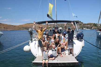 Eine fröhliche Gruppe von Menschen winkt von einem Segelboot aus, umgeben von klarem Wasser und sanften Hügeln.