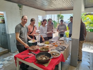 Eine Gruppe von fünf Personen steht um einen Tisch mit verschiedenen Gerichten, während eine Person den Gästen zuschaut.