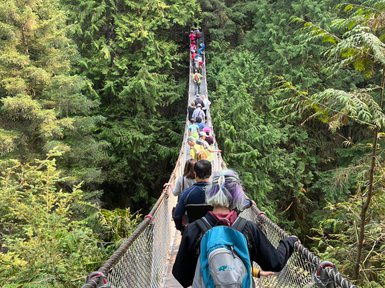 Eine Gruppe von Menschen überquert eine Hängebrücke, umgeben von üppigem, grünem Wald in Lynn Canyon.