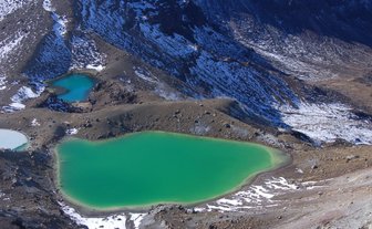 Die beeindruckende Landschaft des Tongariro-Nationalparks zeigt leuchtend grüne Seen, umgeben von schneebedeckten Bergen.