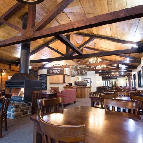 Ein gemütliches Restaurant mit Holztischen und Stühlen, das eine warme Atmosphäre mit einem Kamin und Holzdecken bietet.
