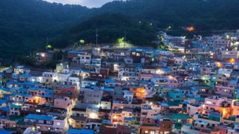 Die bunten Häuser des Gamcheon Culture Village leuchten in der Dämmerung, umgeben von sanften Hügeln und einem klaren Himmel.