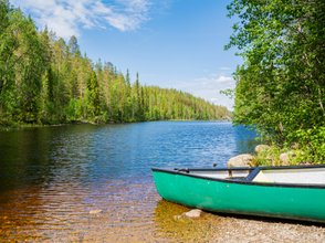 Ein ruhiger See umgeben von üppigem Grün, mit einem grünen Kanu, das sanft am Ufer liegt und die friedliche Landschaft reflektiert.