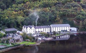 Ein malerisches Hotel am Ufer eines ruhigen Sees, umgeben von üppigem, grünem Wald und sanften Hügeln.