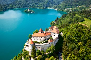 Eine atemberaubende Aussicht auf die Burg Bled, umgeben von üppigem Grün und dem glitzernden Wasser des Sees.