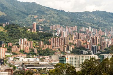 Eine beeindruckende Aussicht auf Medellín, mit hohen Wohngebäuden, die sich an den Berghang schmiegen und üppigem Grün im Vordergrund.