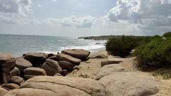 Eine ruhige Küstenlandschaft mit großen Felsen, die am Strand liegen, während sanfte Wellen ans Ufer rollen.