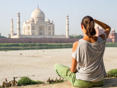 Eine Person sitzt am Ufer und betrachtet das majestätische Taj Mahal, umgeben von einer ruhigen Landschaft.