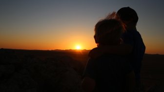 Zwei Kinder blicken gemeinsam auf die untergehende Sonne - Namibia Urlaub mit Kindern